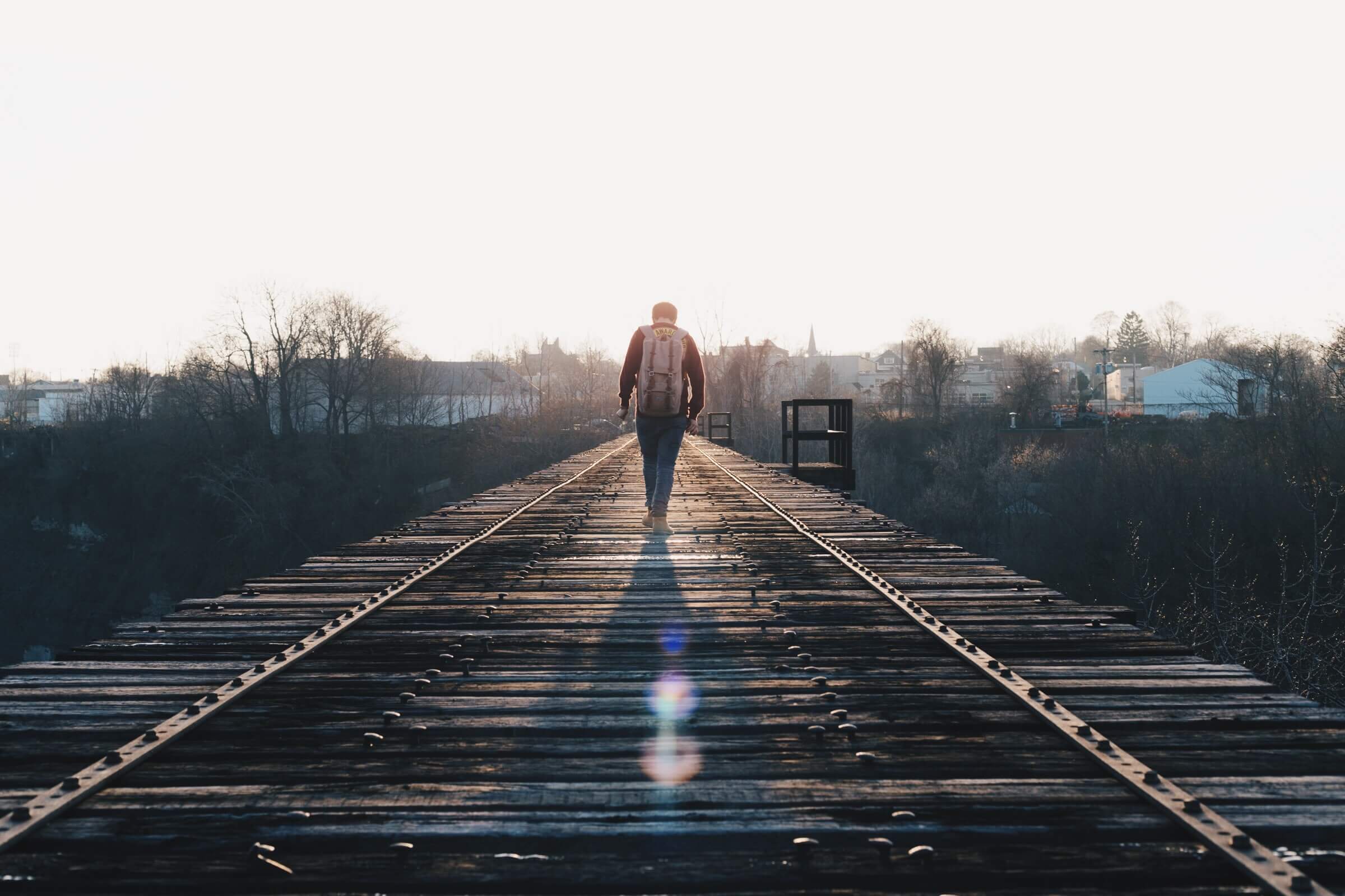 Travelling student walking on a wooden bridge facing the sunset.