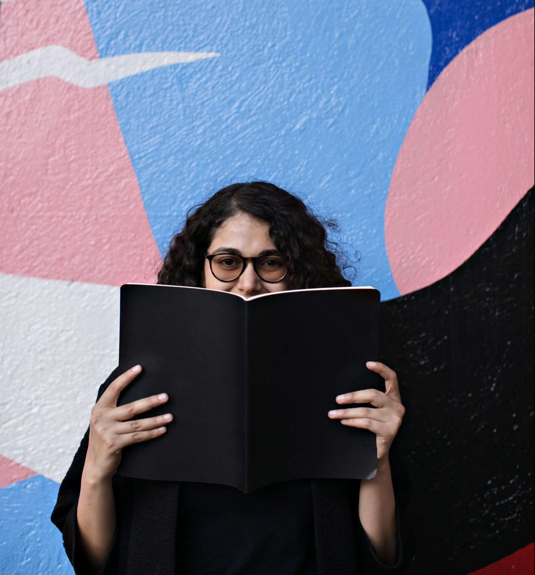 Female college student smiling behind a book.